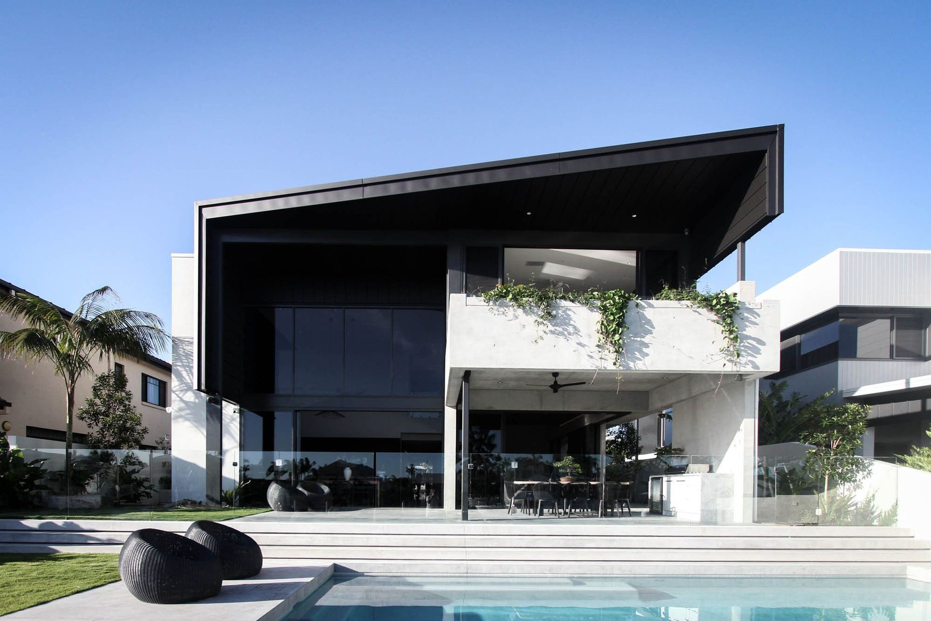 M Residence - Exterior. Dark angular roof floating above the pool and outdoor living.