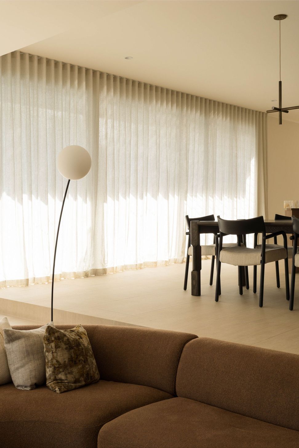 Henderson - Dining Room. Dining chairs and a sculptural floor lamp before sheer curtains.