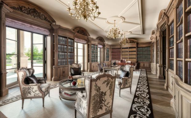 A grand traditional library or study with extensive dark timber built-in bookcases, ornate carved cabinetry, tall glazed doors, decorative ceiling mouldings, and multiple crystal chandeliers. The room contains upholstered armchairs, a central glass-topped table, and a patterned runner, with abundant natural light from tall windows and glazed doors opening to a balcony or terrace.