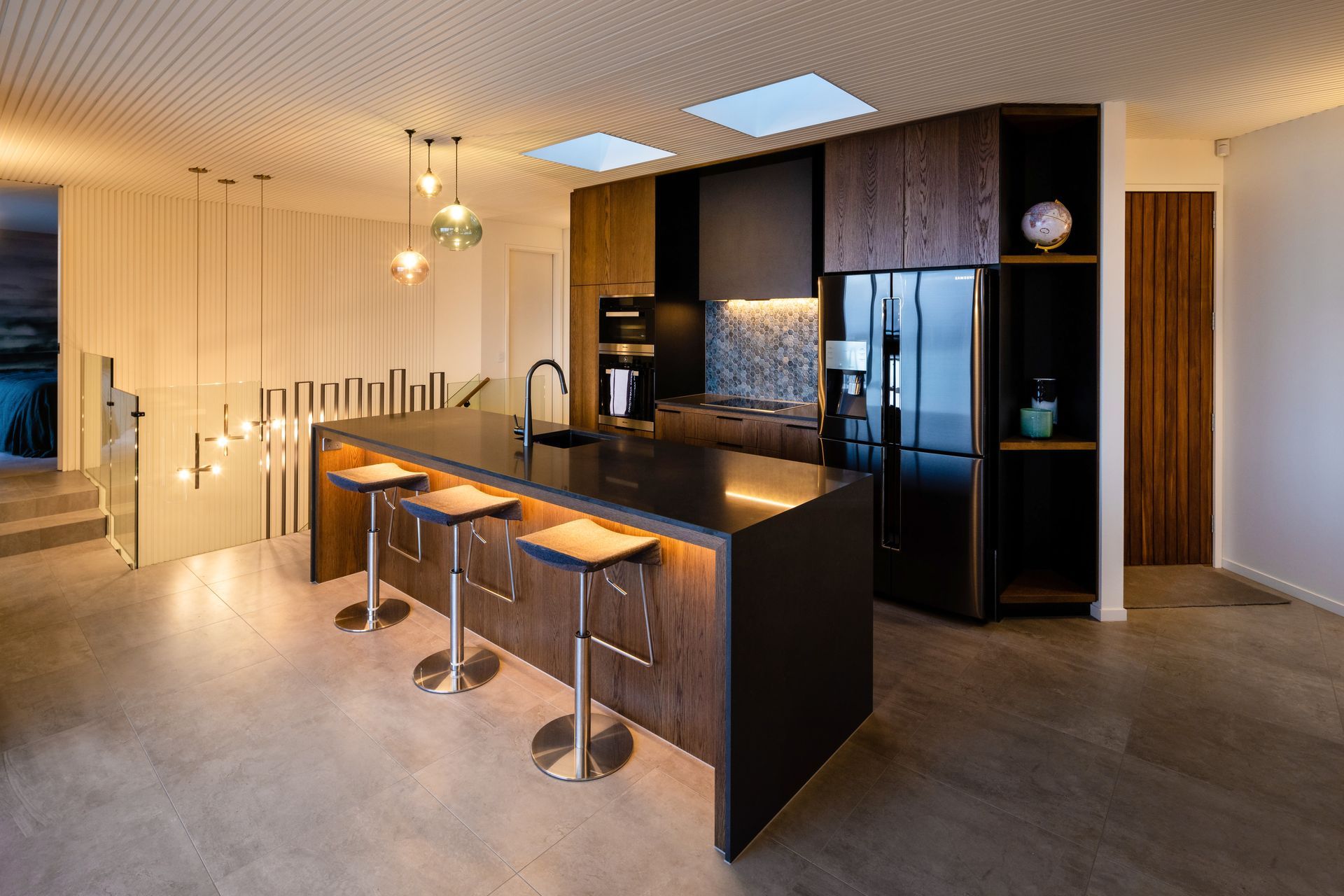 The kitchen features rich timber laminated cabinetry and a routed ceiling surface that leads the eye across the room and down the stairwell.
