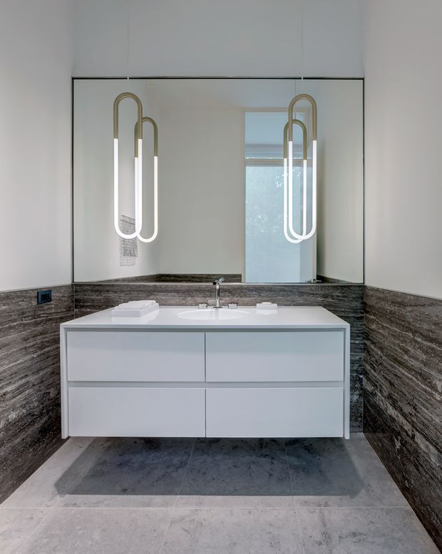 Contemporary bathroom vanity with a floating white double-drawer cabinet, integrated white basin, wall-mounted chrome tapware, large mirrored wall, sculptural vertical pendant lights, dark veined stone wall cladding, and large grey floor tiles.
