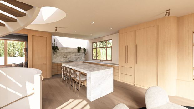 A bright, spacious contemporary kitchen with extensive light timber cabinetry, a large pale stone island with integrated waterfall ends and seating for several people, and a matching stone benchtop along the rear wall. The room includes warm timber flooring, a textured stone splashback, timber-framed windows, recessed lighting, and a sculptural curved ceiling feature with skylight-like openings. A partial freestanding bathtub or curved white fixture is visible in the foreground, but the kitchen dominates the image.