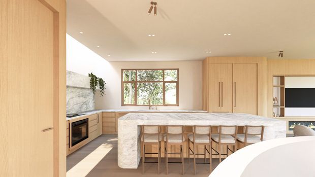 Bright contemporary open-plan kitchen viewed from an adjacent room, featuring extensive light timber cabinetry, a large pale stone island with seating for five or more, integrated appliances, a marble-look backsplash, timber-framed glazing, and recessed ceiling lighting. A living area is partially visible beyond the kitchen.