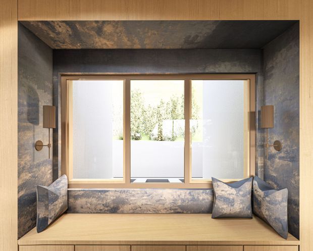 A compact built-in window seat set within a deep, dark textured wall recess. The seat and surrounding cabinetry are light timber, with a long upholstered cushion and matching patterned cushions at both ends. Large timber-framed frosted-glass windows bring in soft daylight, while symmetrical wall sconces flank the opening. The composition is highly tailored and contemporary with a muted, luxurious material palette.