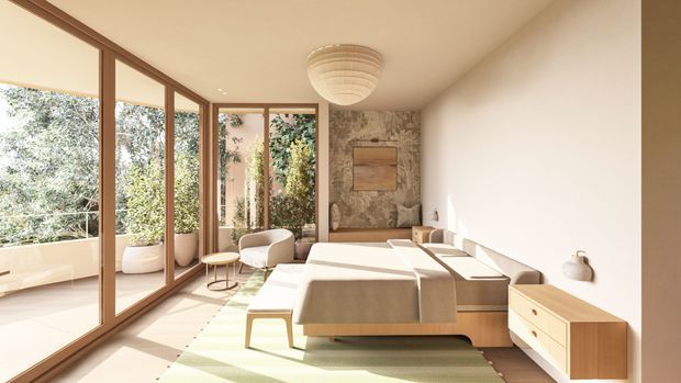 Bright, warm-toned contemporary living room with floor-to-ceiling timber-framed glazing along one side, opening visually onto a planted outdoor area. The room features a large low-profile sectional sofa, light timber media/storage cabinetry, a textured stone or mottled feature wall, a sculptural ceiling light, and a pale striped rug. Natural light and indoor planting create an airy, refined atmosphere.