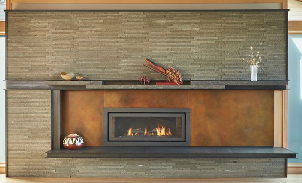 A built-in contemporary fireplace feature wall with a long horizontal gas fire set into a warm rust-toned metal surround. The composition includes dark stone or concrete-look shelving and mantel surfaces, a textured stacked-stone or split-face stone wall finish, and integrated display niches with small decorative objects.