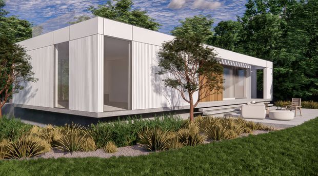 A minimalist single-storey modern home with a crisp flat roof and white vertically ribbed exterior cladding. Large floor-to-ceiling glazed openings and a recessed entry create a strong indoor–outdoor connection. The house is set within a landscaped garden with ornamental grasses, small trees, lawn, and a paved outdoor seating area with a circular fire feature.