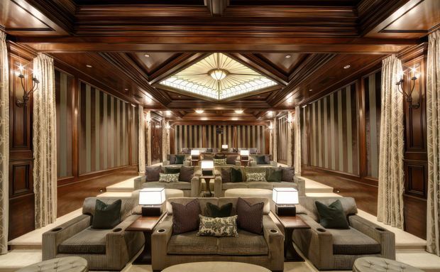 A grand, symmetrical formal living room or lounge with multiple seating arrangements, extensive dark timber wall panelling and coffered ceiling detailing, vertically striped wall panels, ornate sconces, drapery, and a large central stained-glass skylight or ceiling feature. The room has a richly detailed, cinematic and luxurious character.
