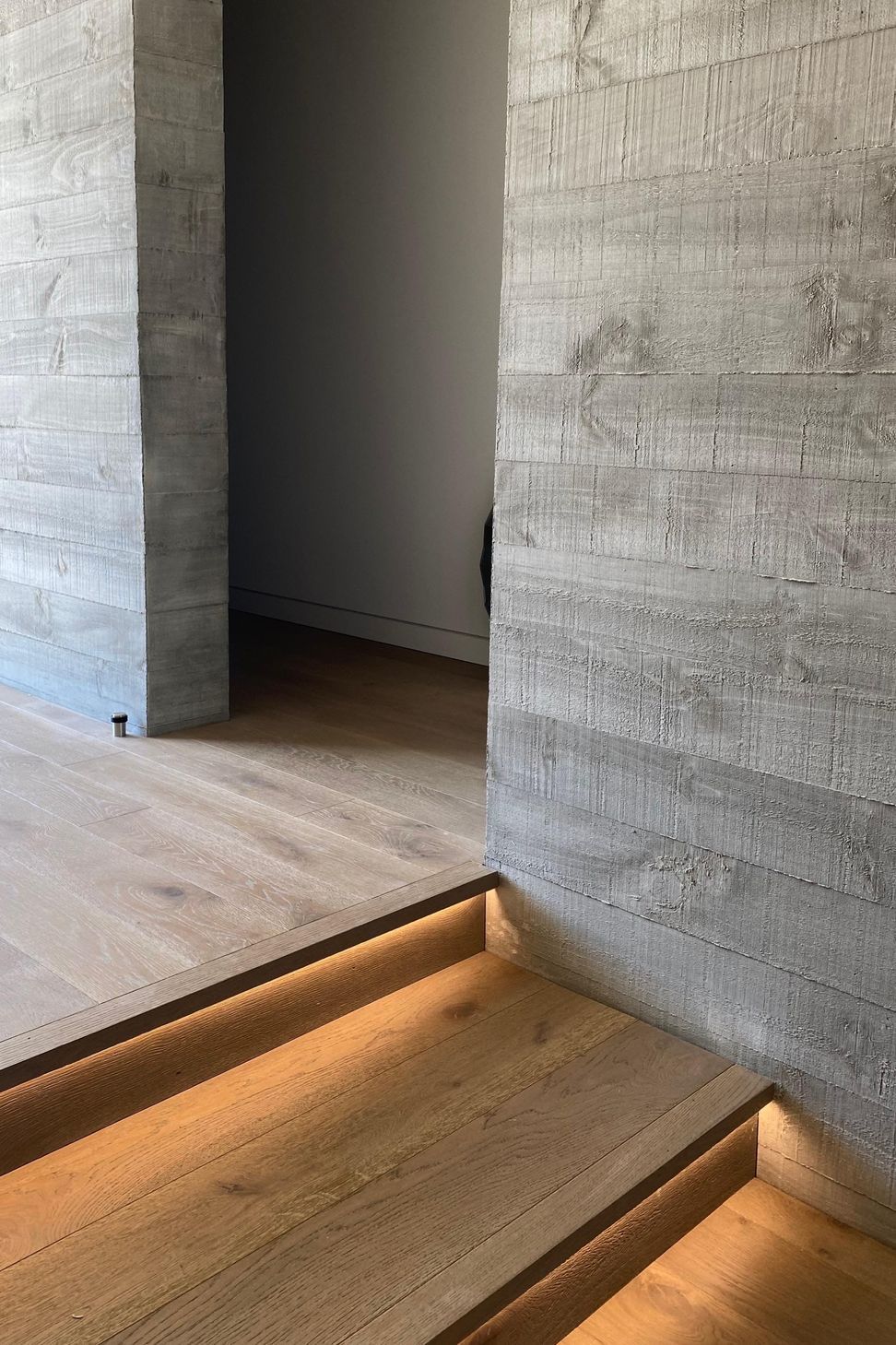 Recessed lighting beneath the stair nosing highlights the warmth of the timber flooring against the concrete walls.