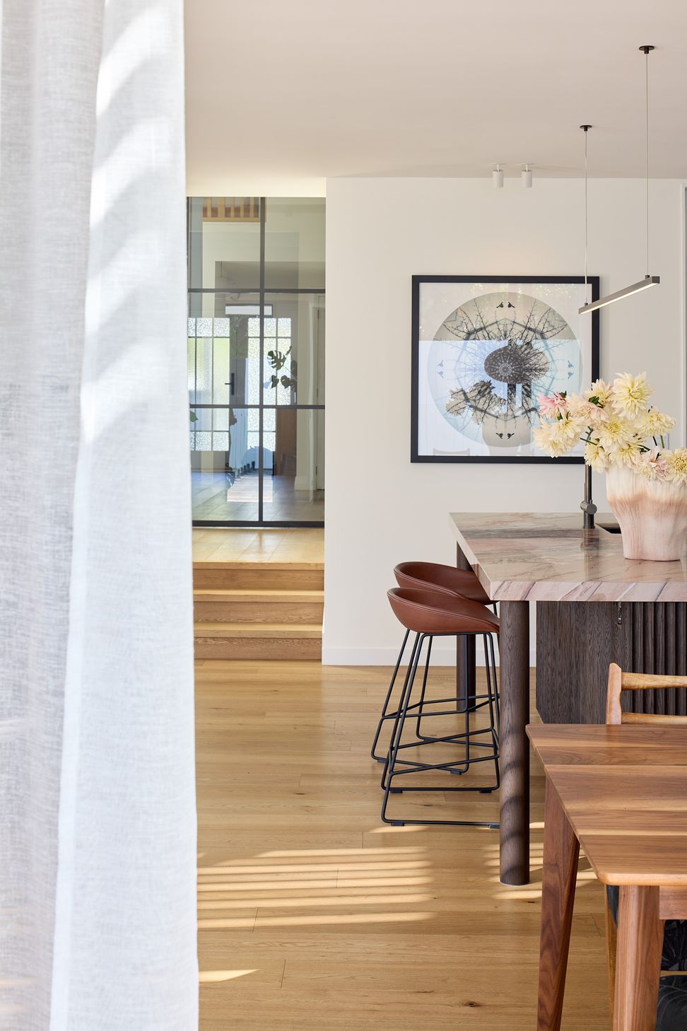 Viewed from the dining area, the open-plan living space celebrates natural materials, with oak flooring, bespoke joinery and steel-framed cavity sliders creating a seamless flow through the home.