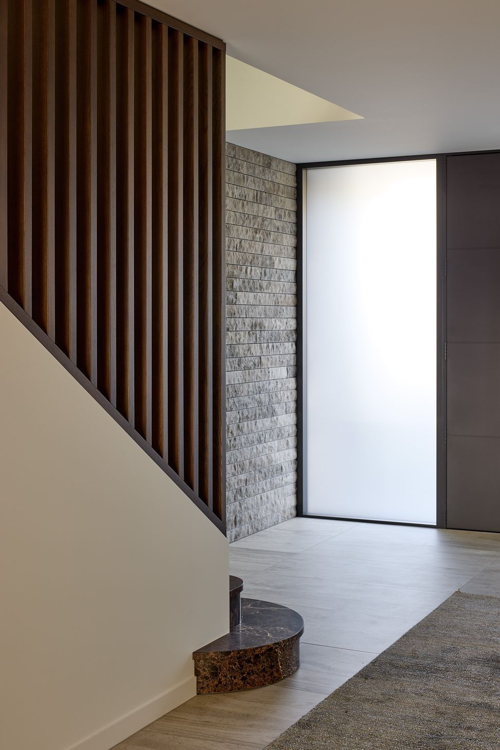 The generous entrance hall introduces the home's refined material palette through tiled flooring, a natural stone feature wall and marble stair treads. A full-height timber screen filters views towards the staircase, while the double-height void creates a strong sense of light and arrival.
