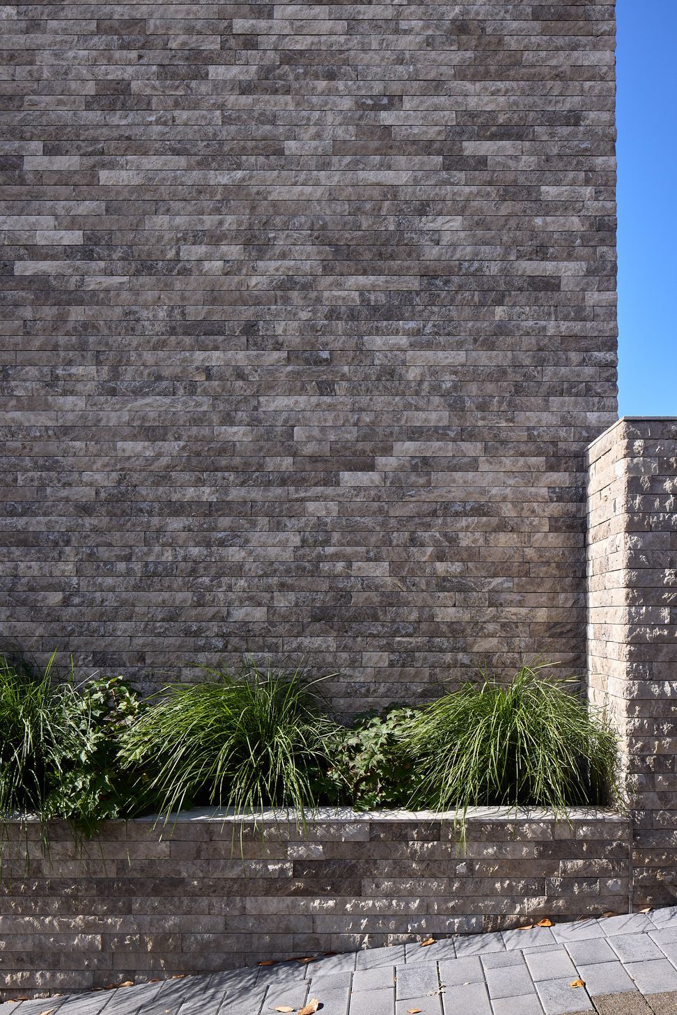 A close-up of the exterior reveals the carefully detailed junction between the house and boundary wall. Stone cladding creates a strong, unified base that grounds the home within its elevated site.
