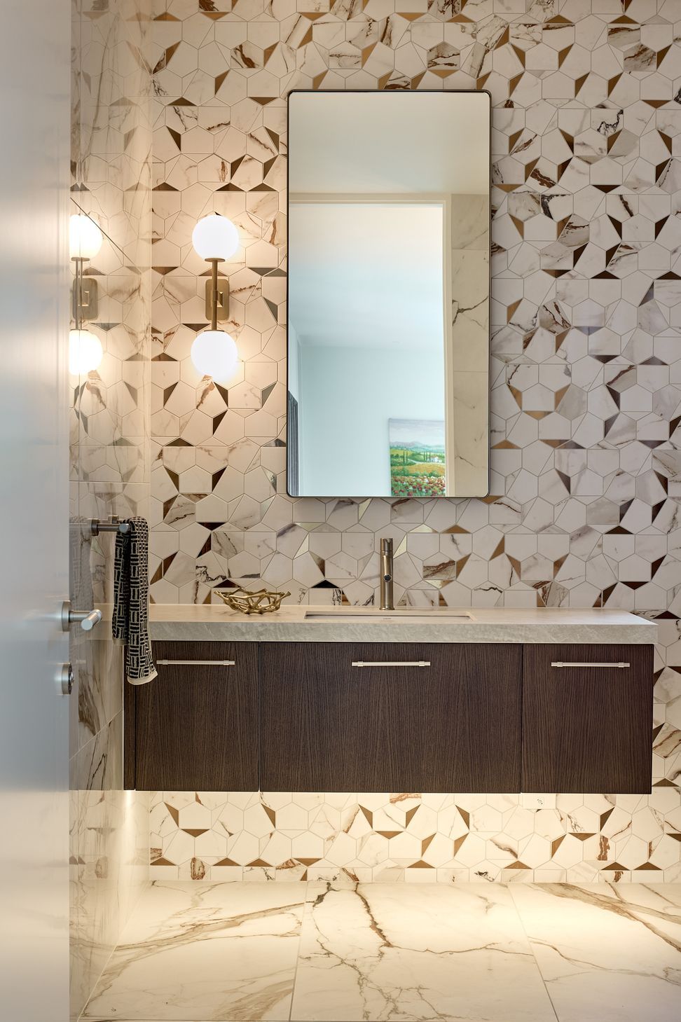 The bathroom combines a bespoke dark timber vanity with a stone benchtop and richly detailed marble-look wall tiles with metallic accents. A carefully selected wall light adds warmth to the refined material palette.
