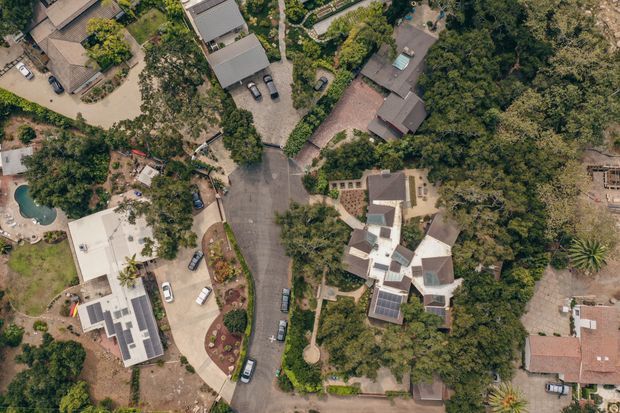 Aerial view of a leafy residential neighbourhood showing several detached homes, landscaped gardens, driveways, parked vehicles, and a curved internal road. One property includes a visible swimming pool and another has rooftop solar panels. The image is dominated by site layout, vegetation, and residential building footprints rather than a single room or facade.