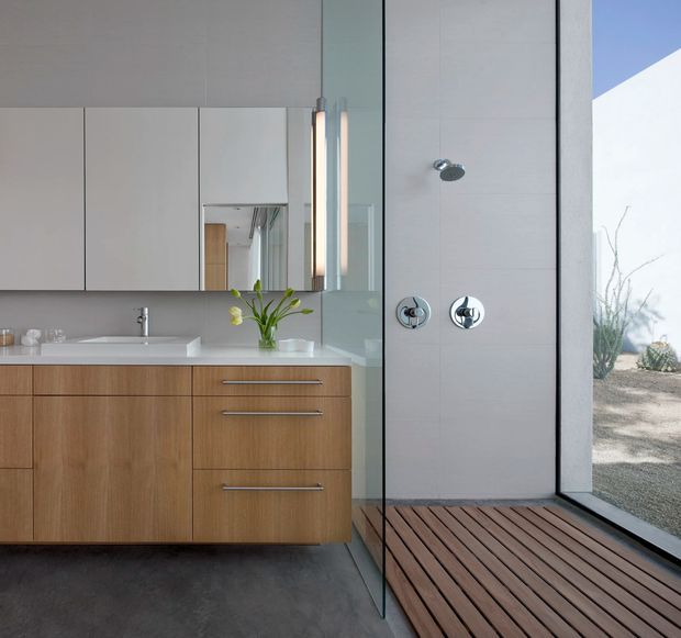 Contemporary bathroom with a floating timber vanity, white countertop and integrated basin, mirrored wall cabinetry, chrome fixtures, a glass-enclosed open shower, and a timber slatted floor beside large glazing overlooking a landscaped exterior.