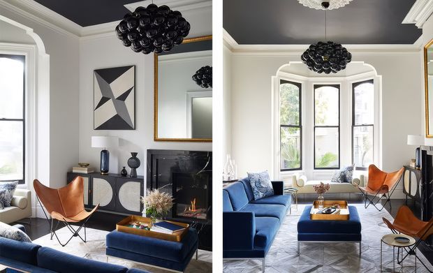 A refined living room shown from two angles, featuring a deep navy ceiling, white architectural trim and bay windows, a black marble fireplace, sculptural black pendant lighting, a blue sofa and ottoman, cognac leather butterfly chairs, a mirrored console, and geometric artwork. The room combines traditional detailing with bold contemporary furnishings.