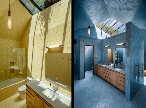 A split-image presentation of two dramatic bathroom interiors. The left bathroom is clad in warm yellow-beige small-format tiles with a skylight, wall-mounted lighting, toilet, shower, and timber vanity with a pale countertop. The right bathroom uses cool blue-grey tiled walls, floor, and ceiling, with a large skylight, timber double vanity, mirrors, wall lighting, and a partially enclosed shower or toilet zone. Both spaces feature strong geometric tile patterns and abundant natural light.