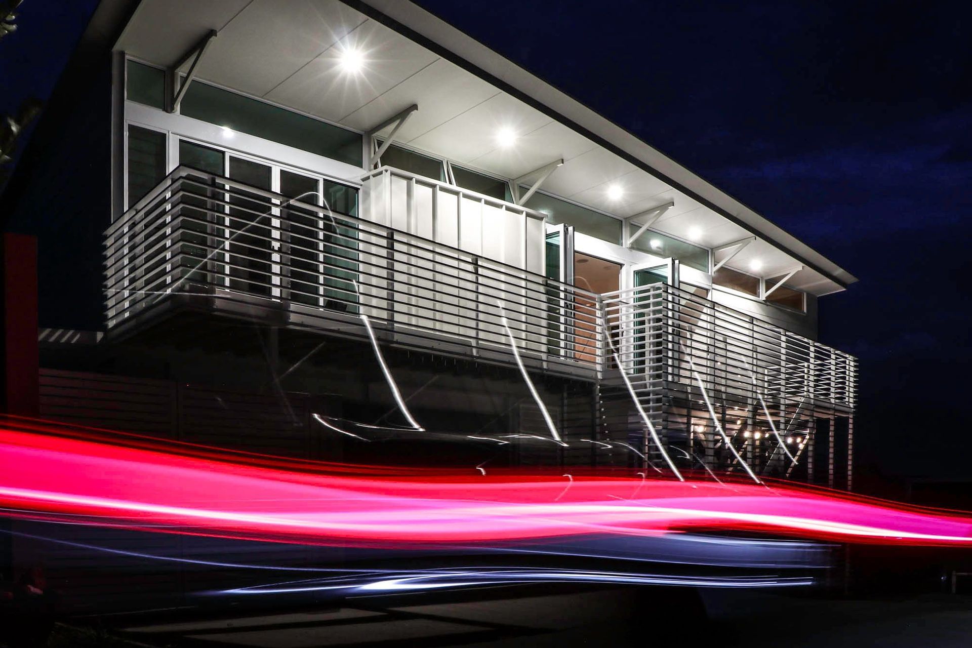 105 Residence - Exterior. Upper deck and slatted screens lit at night with light trails.