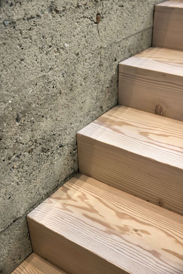 Close-up architectural detail of a compact staircase with thick, light natural timber treads and risers set against a rough exposed concrete or cementitious wall. The image emphasizes the contrast between the warm wood grain and textured grey wall surface; no wider room context is visible.