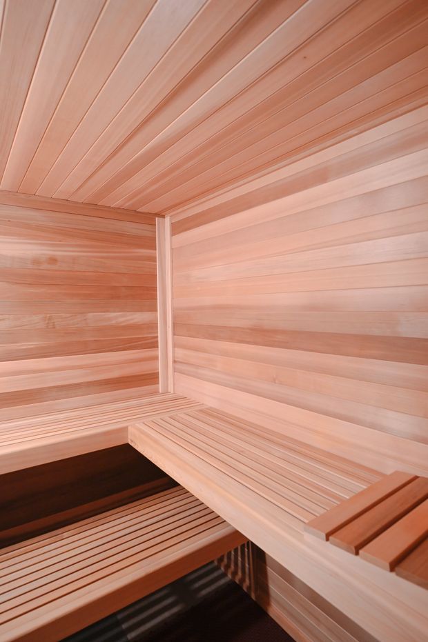 Interior of a compact wood-lined sauna with pale timber wall and ceiling boards, tiered slatted benches, and a warm natural timber finish. The view emphasizes the corner construction, bench layout, and enclosed sauna environment.