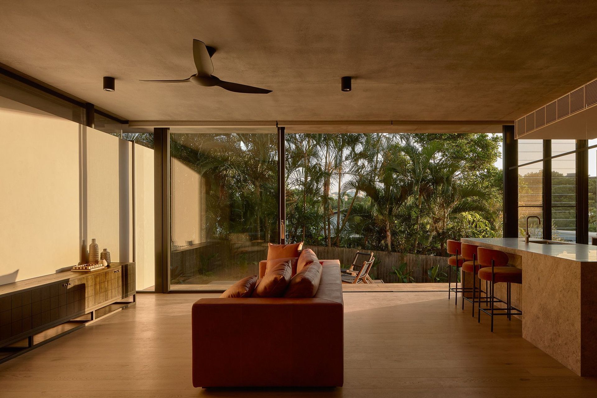 Wildflower Residence - Living Room. Rust coloured sofa facing full height glazing to the garden.