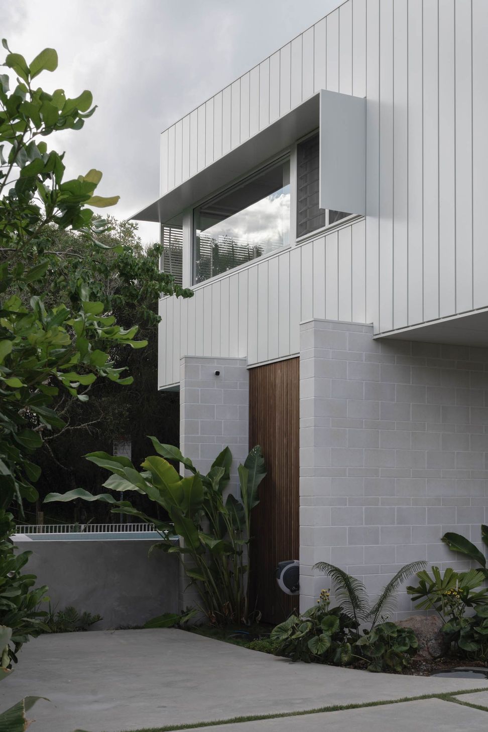 Eleutheria - Entry. Timber entry door tucked between block walls and planting.