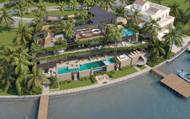 Aerial architectural rendering of a large tropical waterfront residential estate, showing multiple buildings, extensive landscaped gardens, several swimming pools, terraces, outdoor entertaining areas, and a private waterfront edge with a timber jetty. The scheme uses dark pitched and flat roof forms alongside a larger light-coloured multi-storey villa, surrounded by dense palm planting.