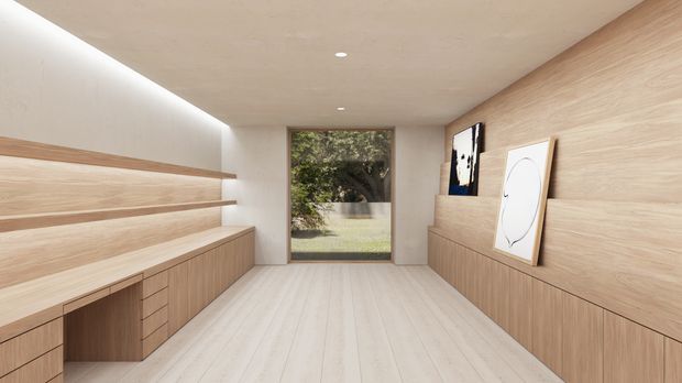 A minimalist, warm-toned interior corridor or dressing area with extensive light timber built-in cabinetry, open shelving, a long low bench, pale timber flooring, and a smooth beige ceiling with recessed lighting. A full-height glazed door or window at the far end opens toward greenery, while framed artwork leans against the timber wall.