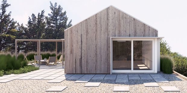 A compact modern gable-roof pavilion or small house clad in vertical weathered timber boards, with large glazed sliding doors and a minimalist gravel terrace. A paved outdoor seating area and landscaped grasses surround the building.