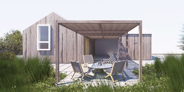 Exterior view of a low-rise contemporary coastal-style home with weathered vertical timber cladding, a simple gabled volume, and a covered outdoor dining terrace. The terrace has a timber-framed flat pergola, paved deck, glass-topped dining table, and outdoor chairs, surrounded by ornamental grasses and low planting.