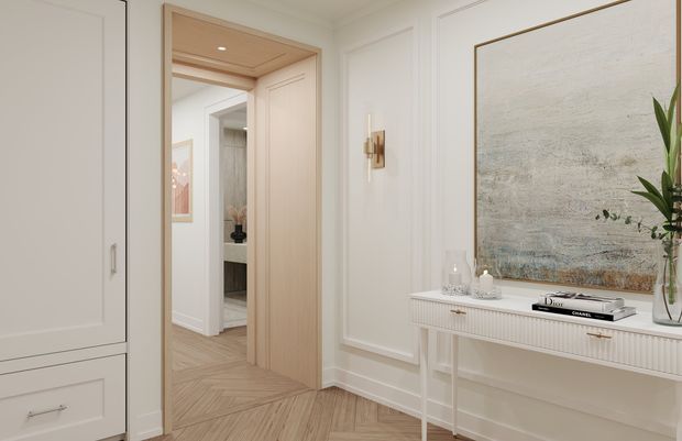 Bright refined hallway or entry space with white decorative wall panelling, pale timber herringbone flooring, a light timber-lined doorway, and built-in cabinetry. A slim fluted-front console sits beneath a large textured abstract artwork, with understated brass-toned lighting and decor. The doorway opens toward another interior area with additional cabinetry and a glimpse of artwork.