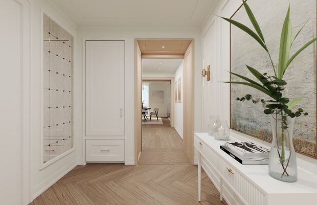 A bright, refined residential hallway with white paneled walls and trim, herringbone timber flooring, built-in white cabinetry, and a white console with decorative objects and a tall indoor plant. A framed artwork, wall sconces, recessed lighting, and a timber-lined doorway lead toward a dining or living area beyond.