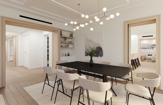 Bright, refined dining room with a large dark rectangular dining table surrounded by upholstered dining chairs. The room features light timber flooring, pale neutral walls, decorative wall moulding, wide trimmed openings to adjoining rooms, built-in open shelving, and a sculptural multi-globe pendant chandelier. Contemporary artwork and a vase provide restrained decoration. Additional hall and living areas are visible through the openings.