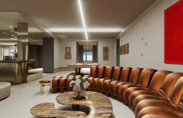 A sophisticated contemporary living room with a large curved caramel-brown leather sectional sofa arranged around an organic-shaped stone coffee table. The room includes a compact bar or kitchenette with dark cabinetry and reflective surfaces, a dining or console area in the background, recessed linear ceiling lighting, pale walls and flooring, and colourful wall artwork. The space has a polished, luxurious and dramatic atmosphere.