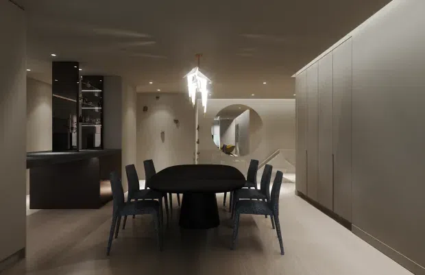 A sophisticated open-plan dining area with a dark oval dining table and black upholstered chairs, positioned between a dark kitchen island and tall minimalist cabinetry. The room features warm neutral finishes, concealed storage, recessed lighting, a sculptural pendant light, and a large arched opening leading toward another space. The overall presentation is refined and contemporary with a moody, monochromatic palette.