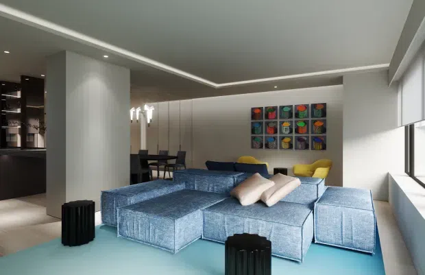 Contemporary open-plan living room with a large blue modular sectional sofa, pale cushions, and a vivid blue floor covering. The room has a minimalist recessed ceiling with integrated lighting, full-height windows along one side, dark built-in cabinetry at the rear, a dining area, yellow occasional seating, and a colourful grid artwork on the back wall.