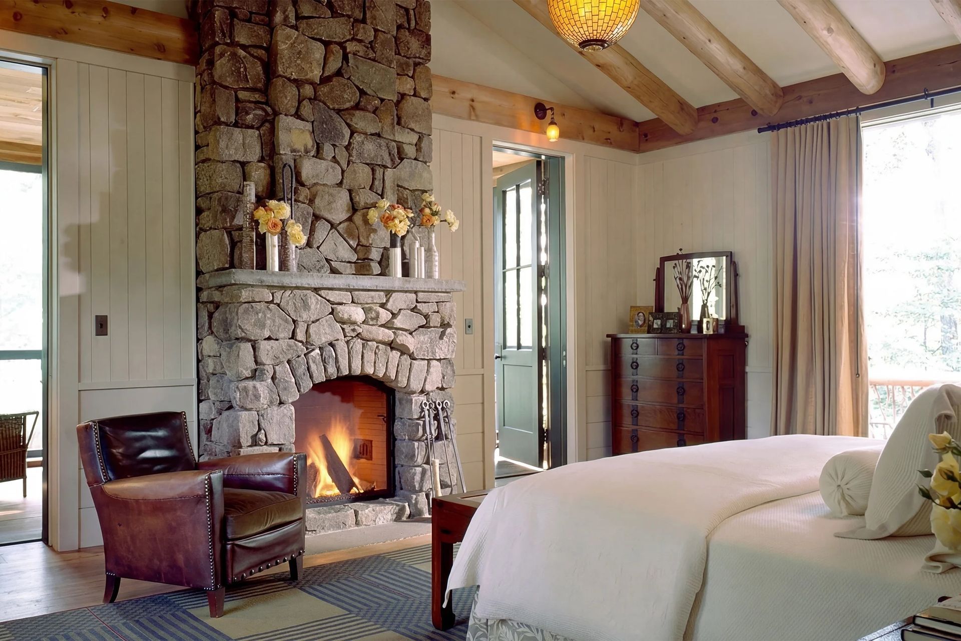 adirondack-lodge-primary-bedroom-stone-fireplace-timber-beams-interior-design-architect-ap-compressed.jpg