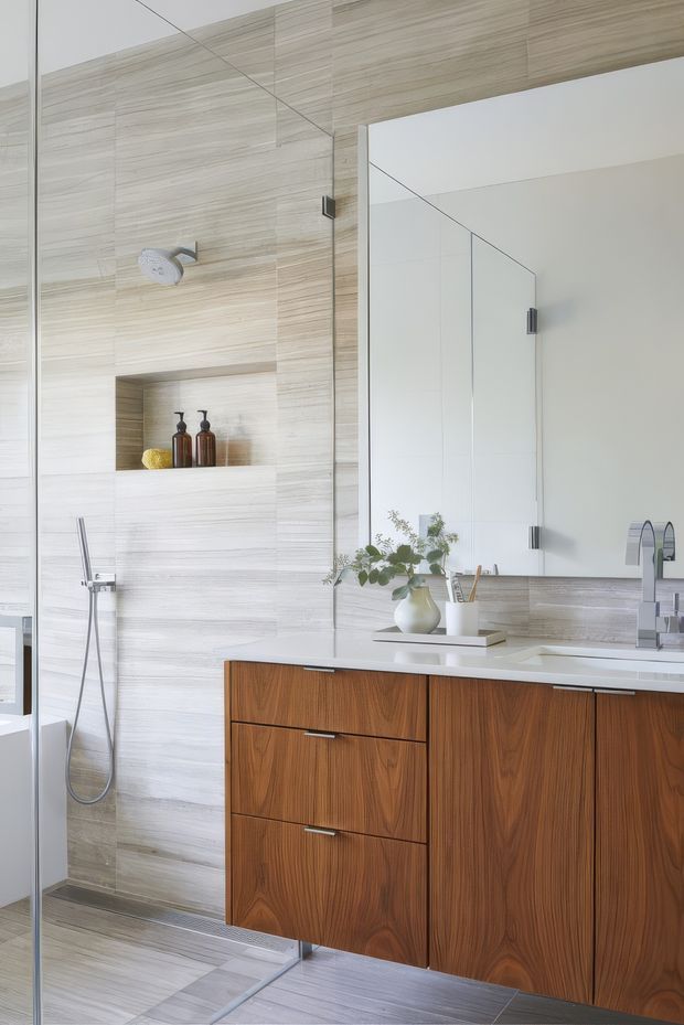 Bright, refined contemporary bathroom featuring full-height light wood-look tiled walls and matching floor tiles, a frameless glass shower enclosure with recessed niche, wall-mounted timber vanity with integrated white countertop and basin, large mirrored cabinet, and brushed metal tapware. Natural wood cabinetry and minimal accessories add warmth to the clean, modern space.
