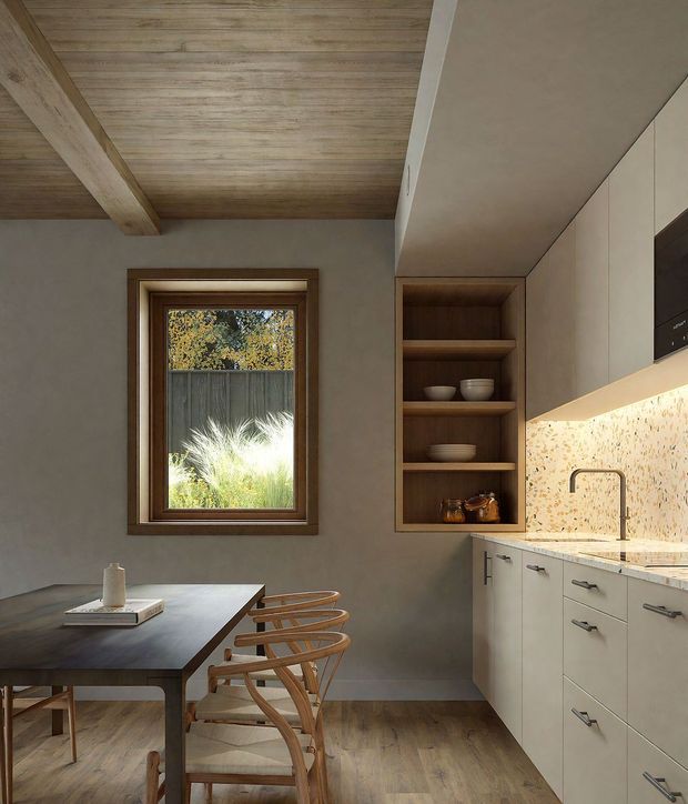 Warm, refined kitchen-dining interior with pale timber flooring, a dark timber dining table and curved timber chairs, light cabinetry, a speckled stone backsplash and benchtop, and an integrated dark appliance. The room features a timber-lined pitched ceiling with exposed beams, a timber-framed window, and open timber shelving. Natural light and greenery visible outside create an inviting atmosphere.