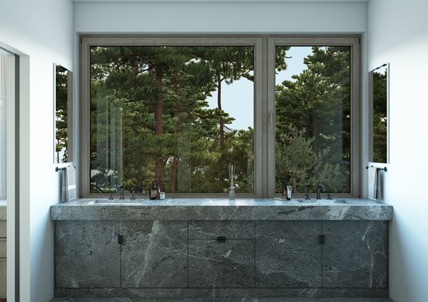 A contemporary bathroom vanity positioned beneath a large two-part window overlooking dense pine trees. The wall-mounted vanity has a dark grey veined stone benchtop and matching slab-front cabinetry, with two integrated basins, wall-mounted taps, mirrors at both sides, and a bright white surrounding interior.