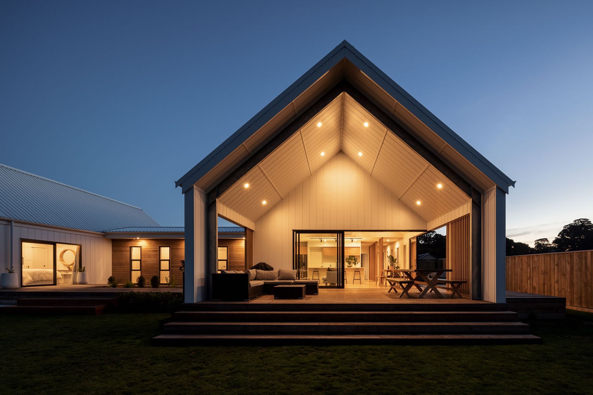 A large stacking slider, along with a level threshold, dissolves the division between inside and the covered living space that terraces down to the lawn and is covered with a large gabled void extruded from the main roof.