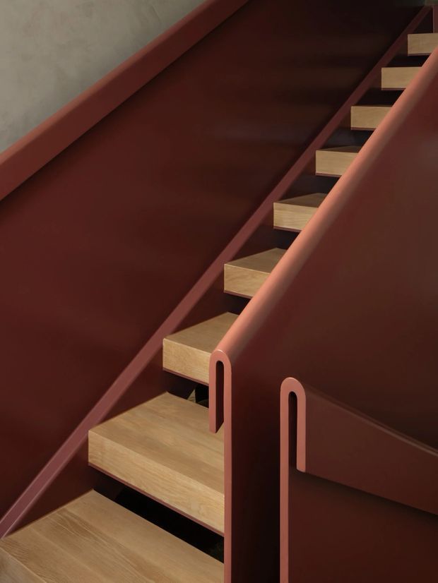 Close-up architectural photograph of a contemporary stairway with floating light timber treads set within deep red-brown painted side panels and balustrades. The sculptural stair enclosure has rounded cut-out handrail details and strong diagonal geometry, creating a refined, dramatic interior composition.