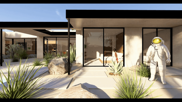 A contemporary single-storey courtyard-style building with a flat roof, pale rendered walls, extensive black-framed glazing, and a paved outdoor forecourt. Drought-tolerant ornamental grasses, agave-like plants, and large rocks landscape the space, while an astronaut sculpture stands near the entrance. Strong sunlight creates crisp shadows across the paving and facade.