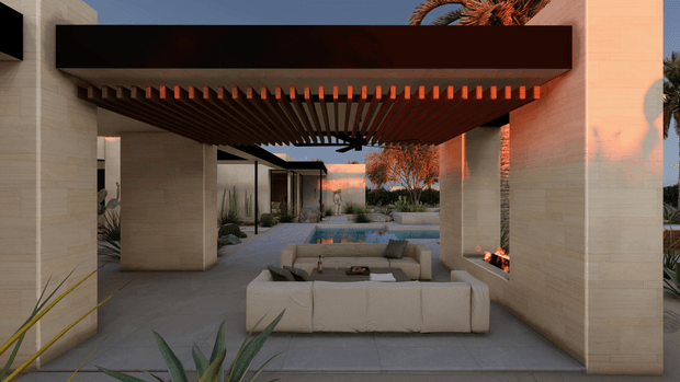 A modern outdoor living area beneath a broad dark timber pergola, framed by pale stone or concrete-clad columns and walls. The space includes a large upholstered sectional seating arrangement around a low coffee table, an integrated linear fire feature at the right, and a small reflecting or plunge pool beyond. Desert-style planting, sculptural palms, and warm sunset light create a refined resort-like courtyard atmosphere.